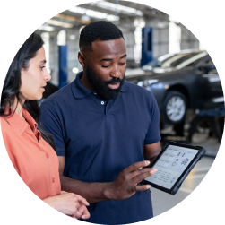 Service director in auto dealership body shop showing data to customer on tablet